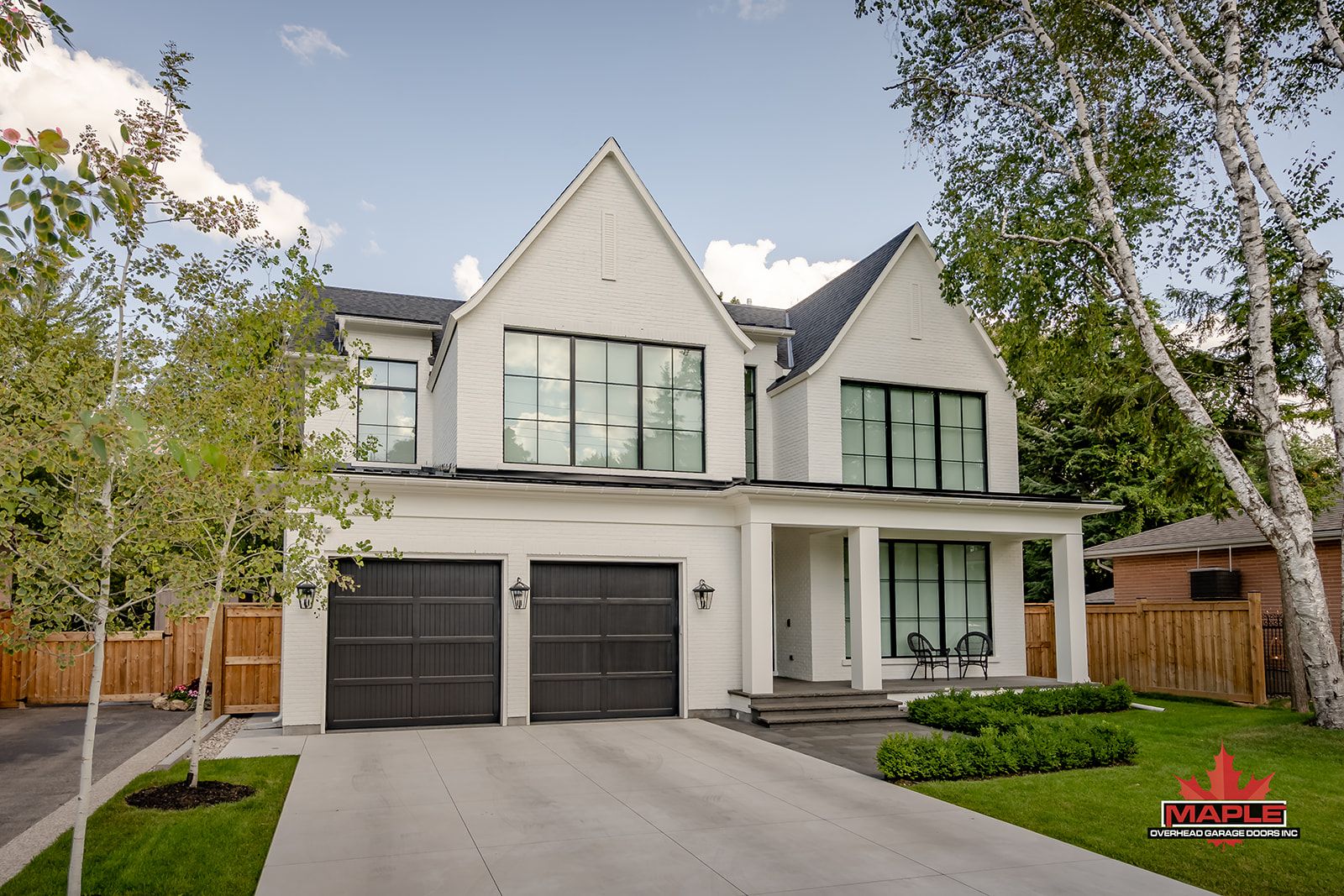 A large white house with two black garage doors and a large driveway.