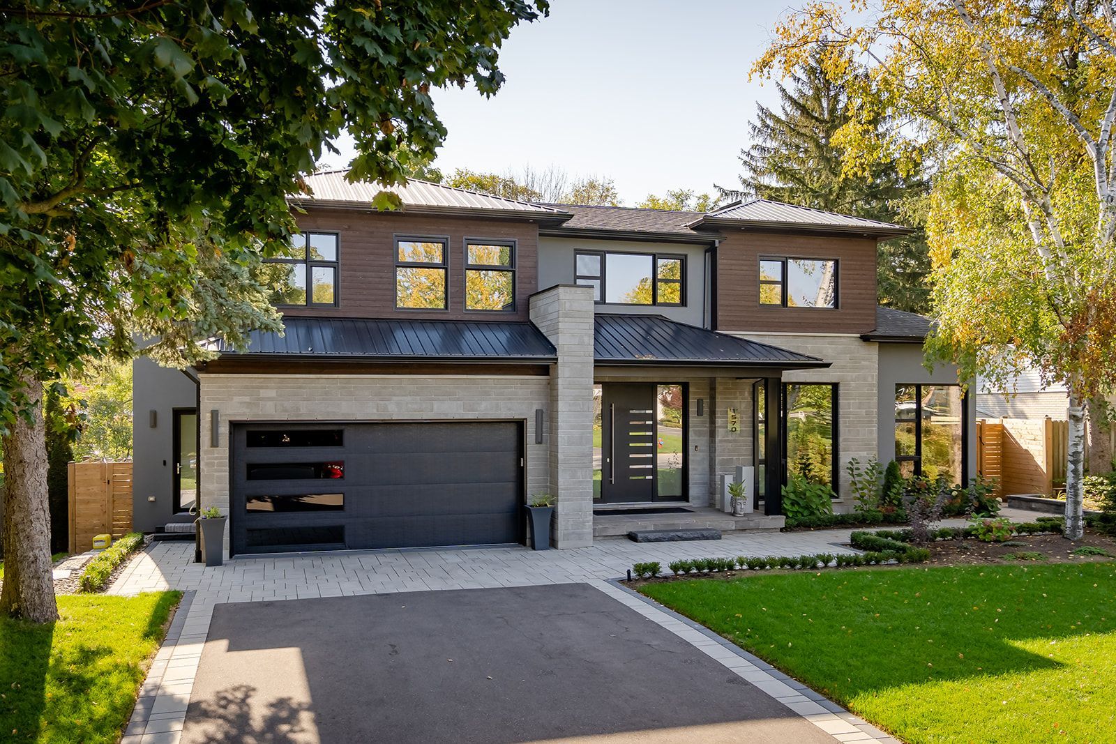 A large house with a black garage door is surrounded by trees and grass.