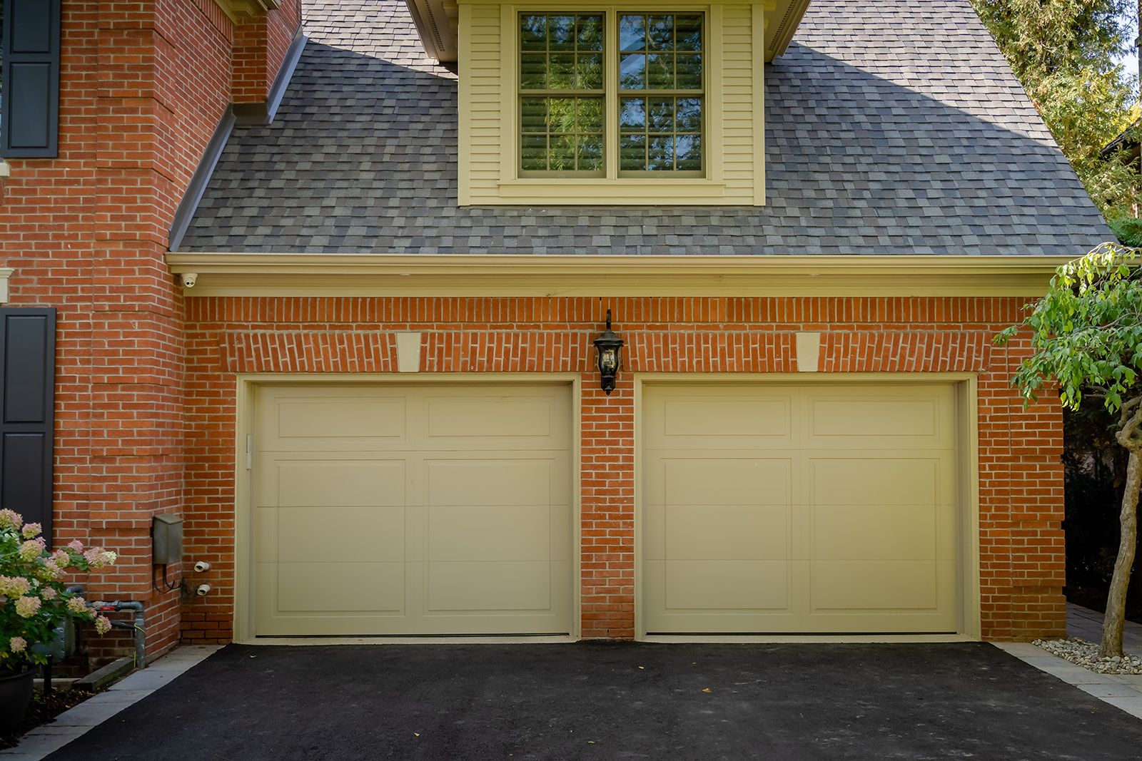 A brick house with two garage doors and a black driveway.