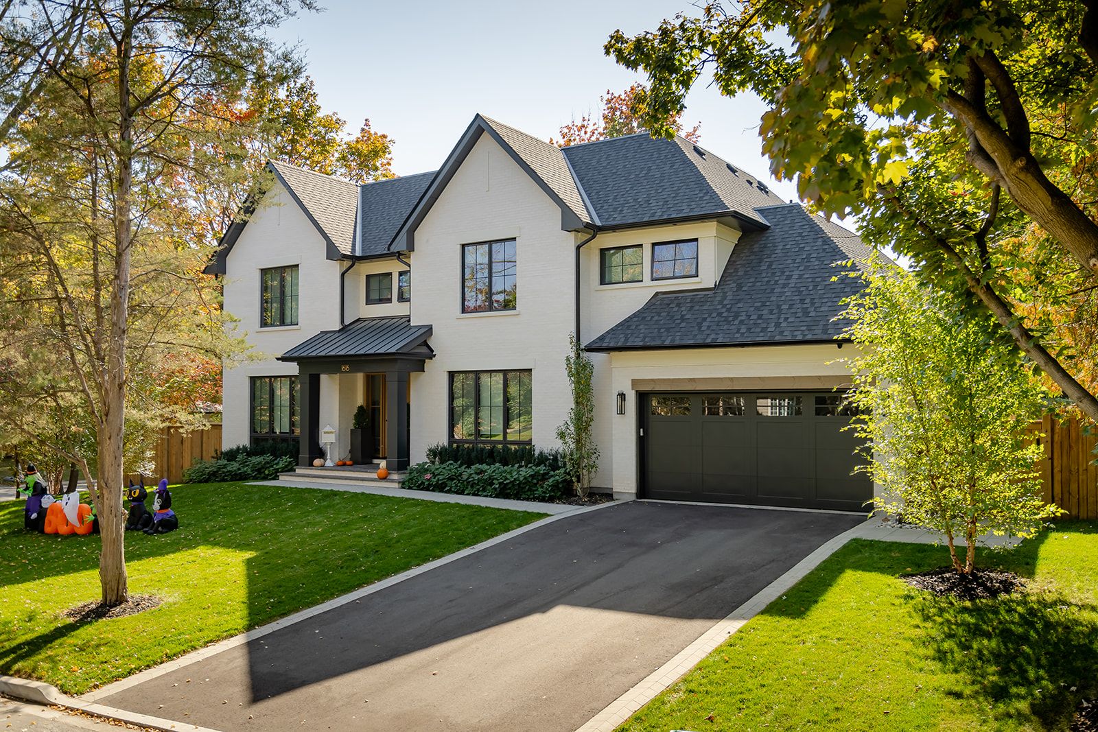 A large white house with a black garage door is sitting on top of a lush green lawn.