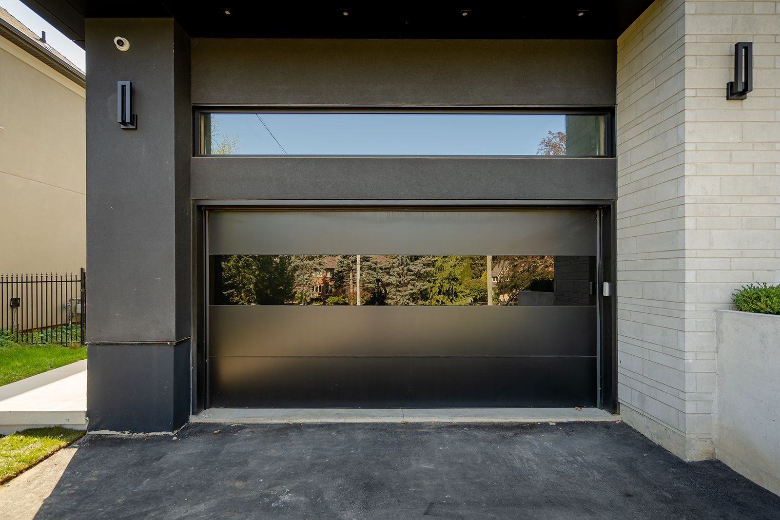 A black garage door with a large window is in front of a house.