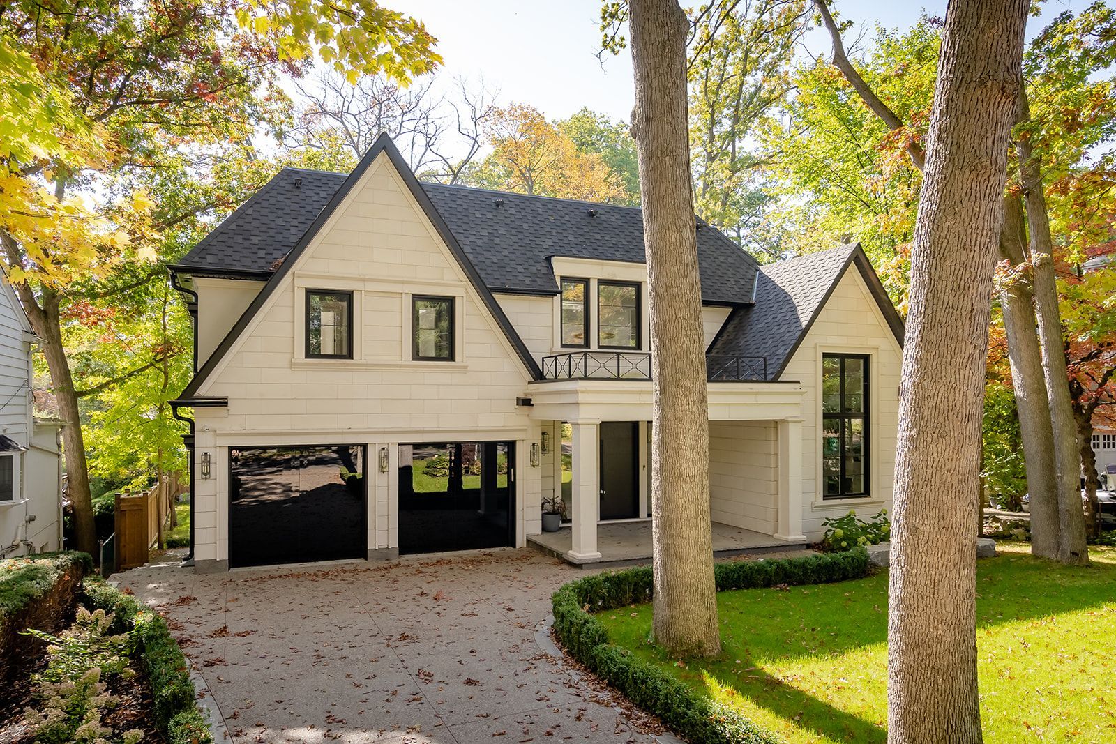 A large white house with a black garage door is surrounded by trees.