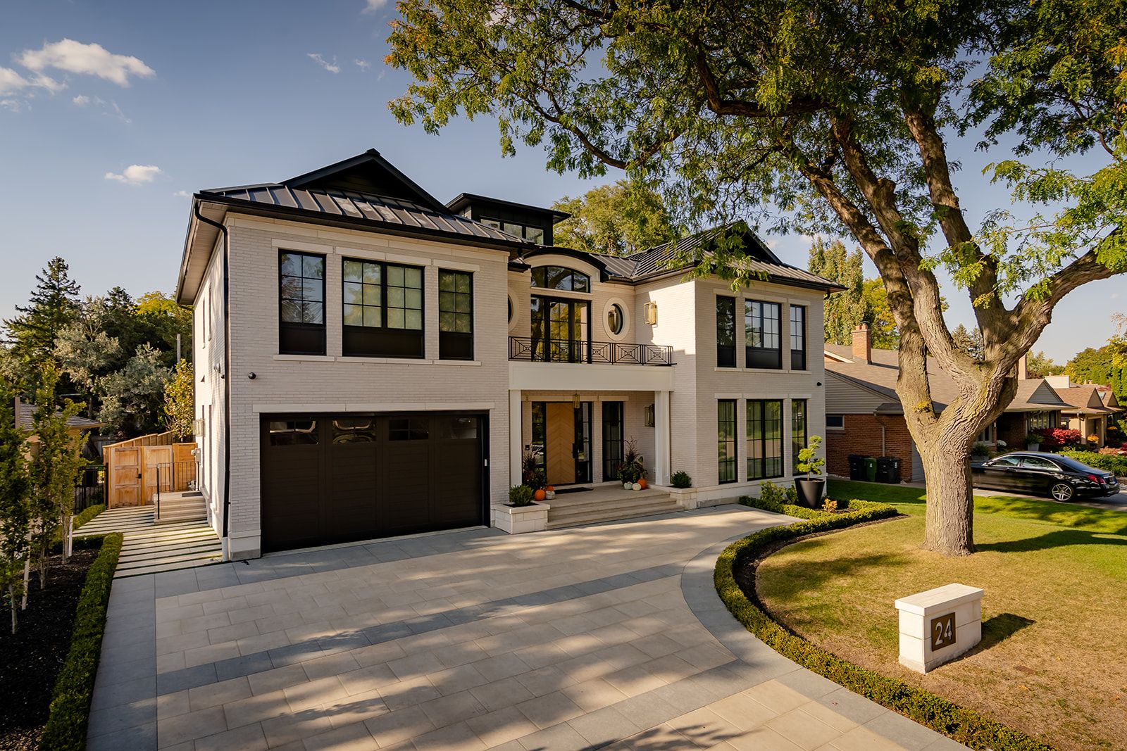 A large white house with a black garage door and a tree in front of it.