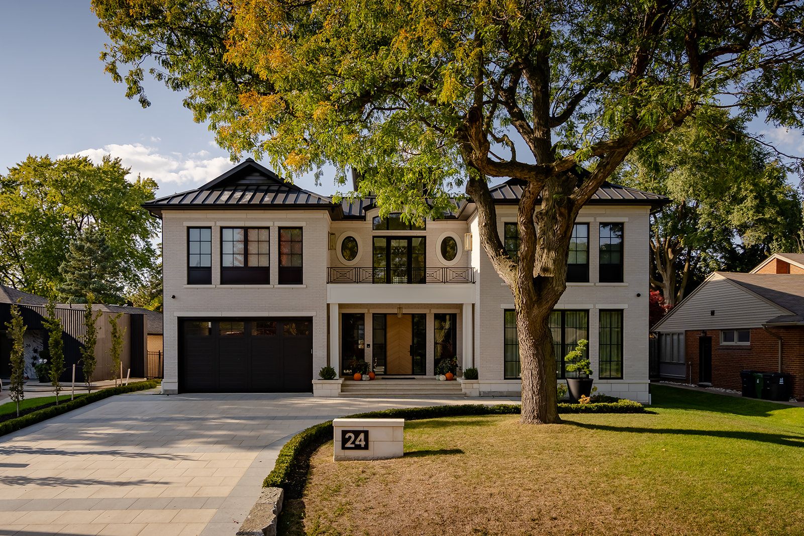 A large white house with a black garage door and a tree in front of it.
