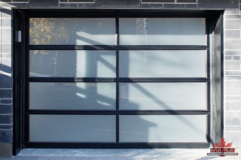 A black garage door with a brick wall behind it