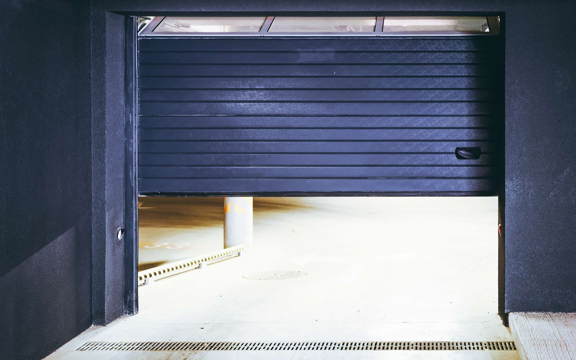A black garage door is open in a parking garage.