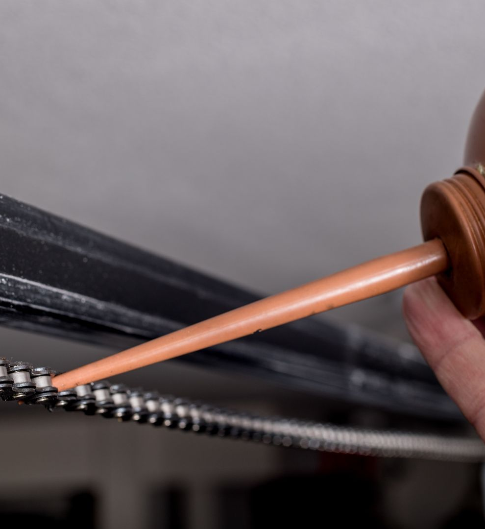 Hand oiling a garage door opener chain with a brown oil can.