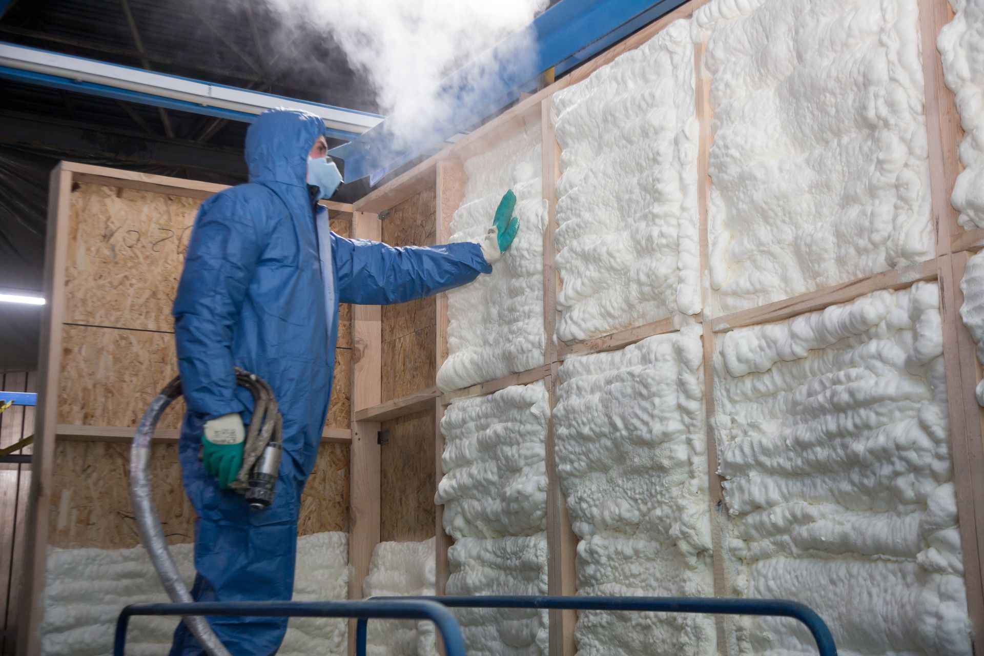 A man in a blue suit is spraying foam on a wall.