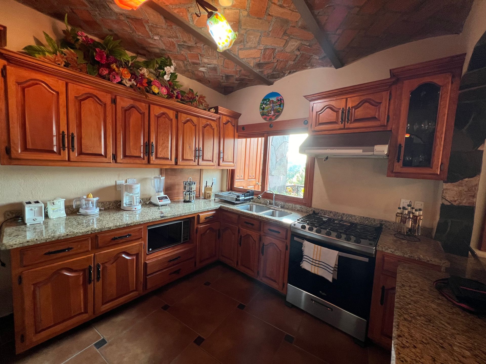Una cocina con gabinetes de madera, encimeras de granito, una estufa y un fregadero.