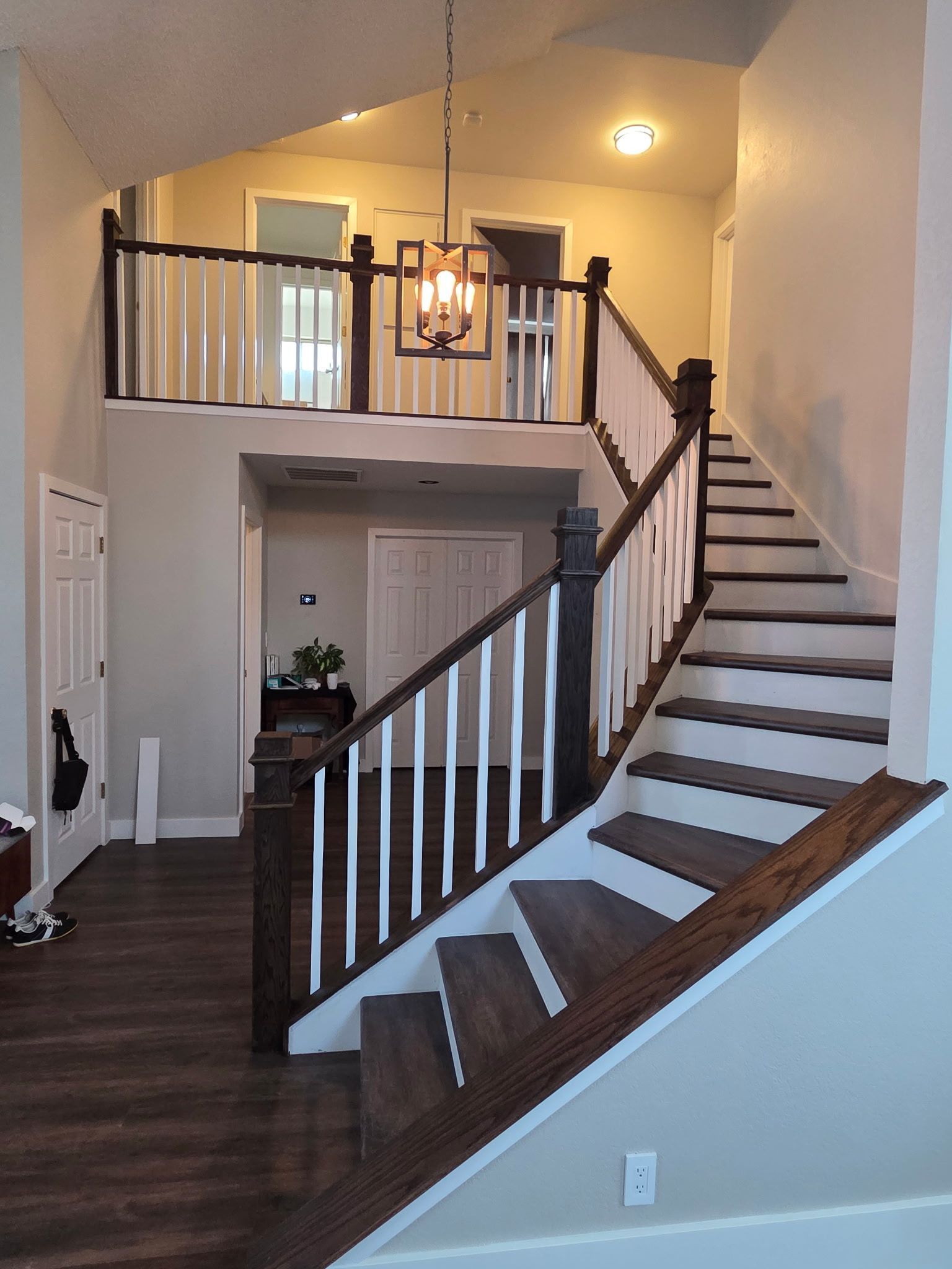 A wooden staircase leads to a loft with bookshelves, and a dining area below with large windows.