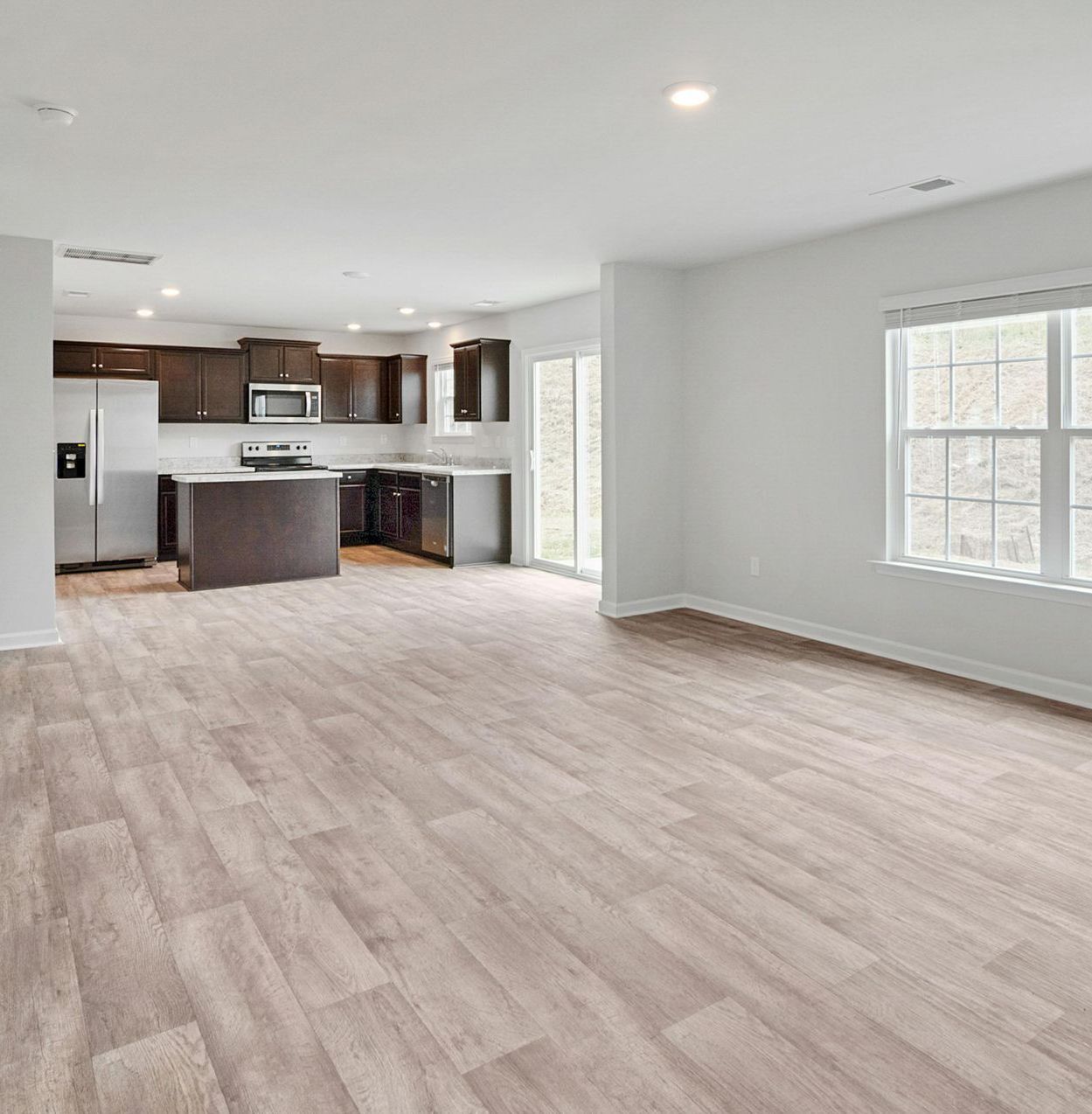 An empty living room with hardwood floors and a kitchen in the background.