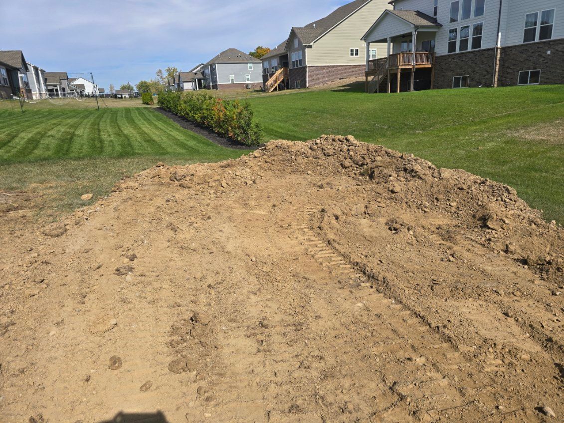 Pile of dirt in a grassy yard, houses in the background on a sunny day.