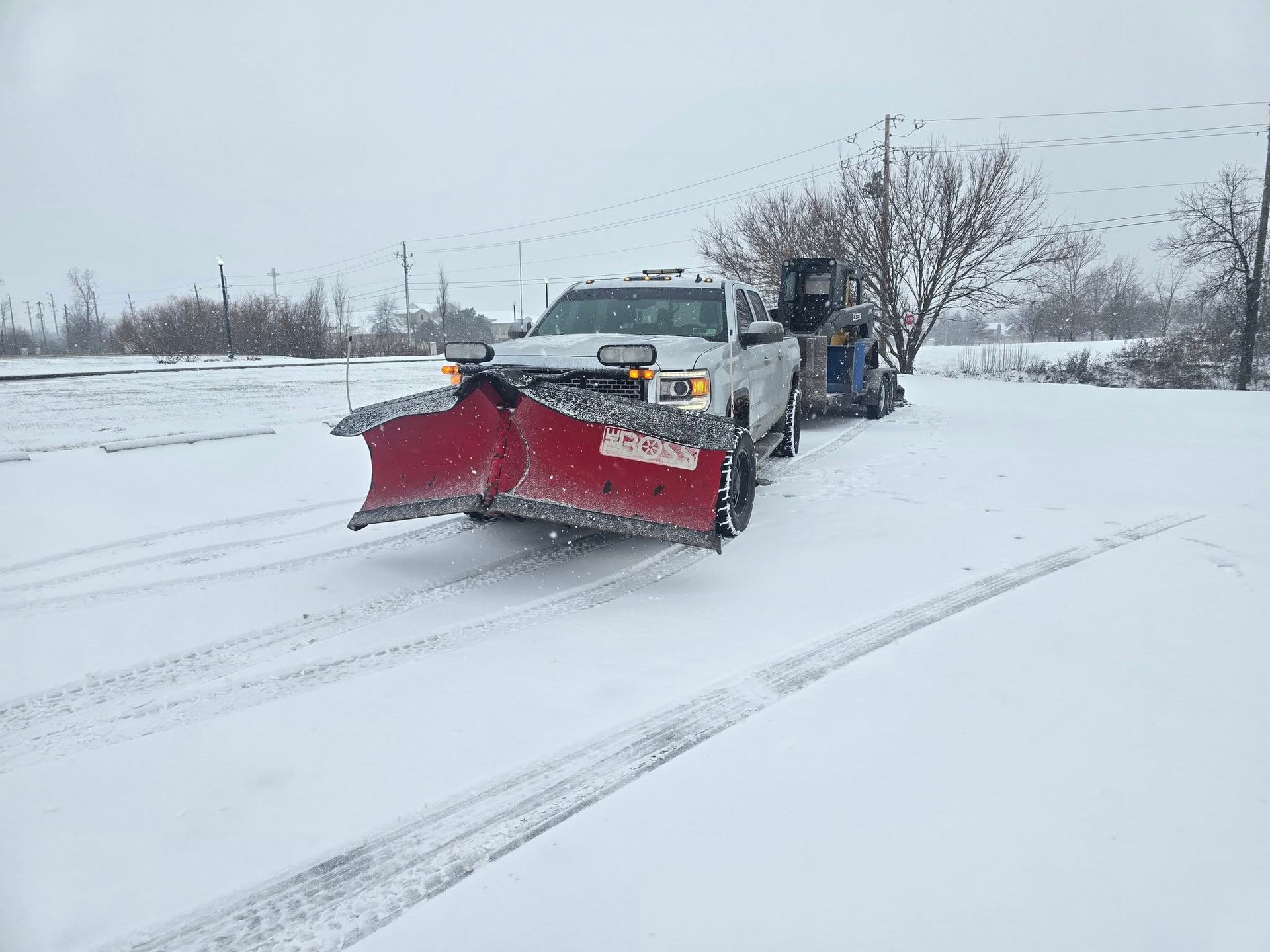 Snowplow truck plowing a snow-covered road during a snowfall.