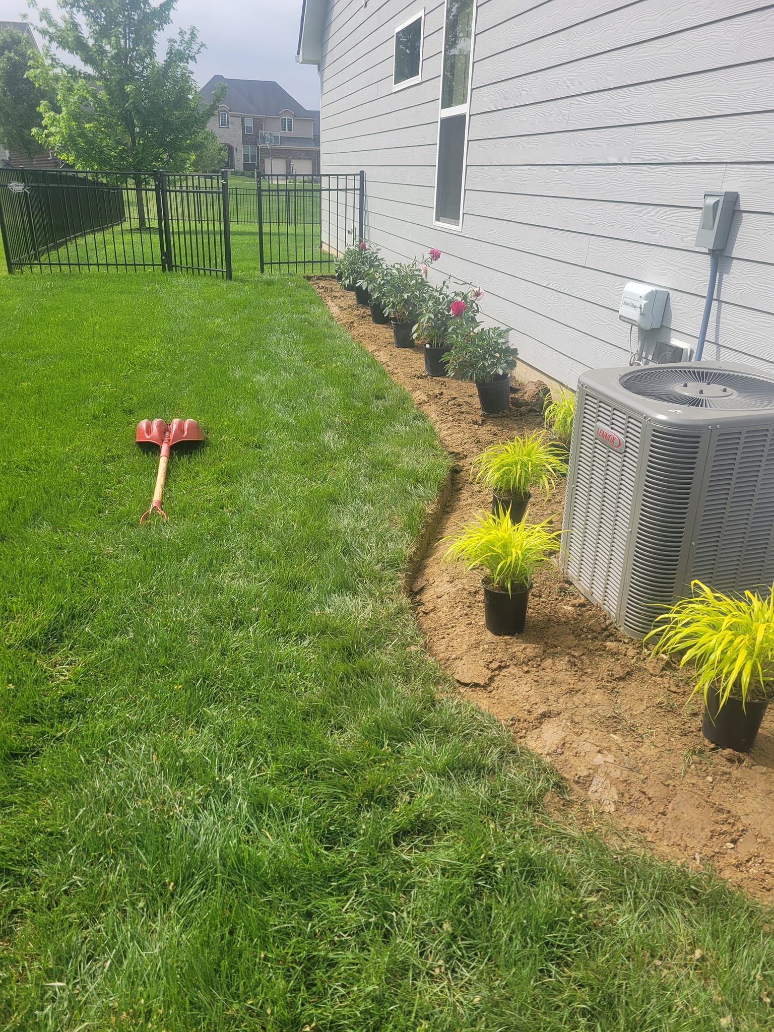 A yard with newly planted flowers along a house, a rake sits on the lawn.