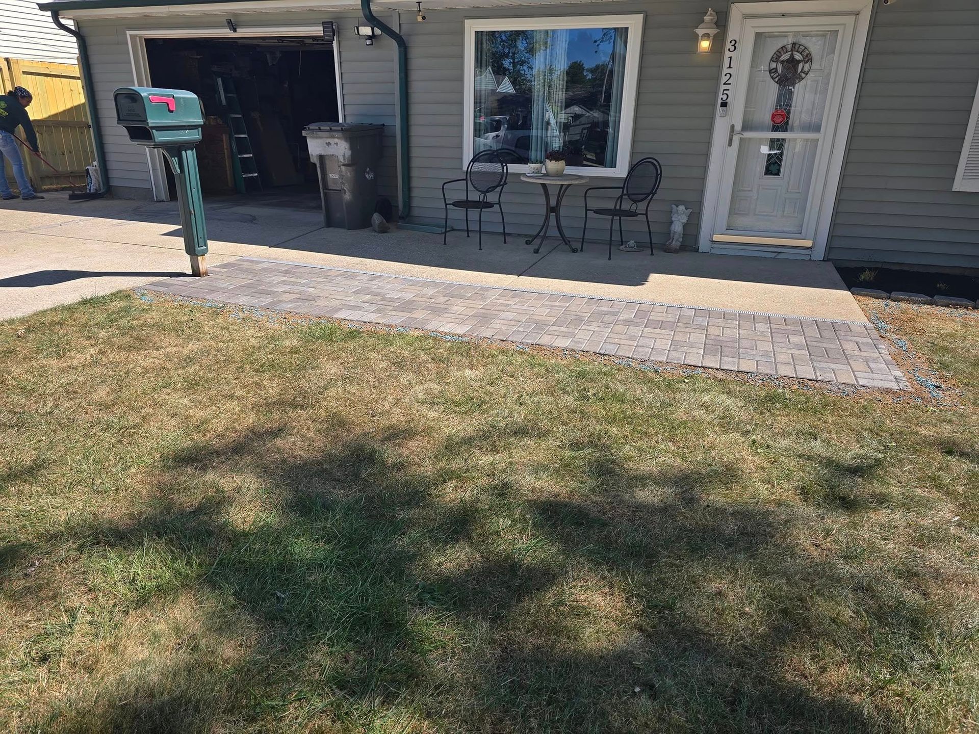 A house with a patterned walkway leading to the front door. A table and chairs sit on the porch.