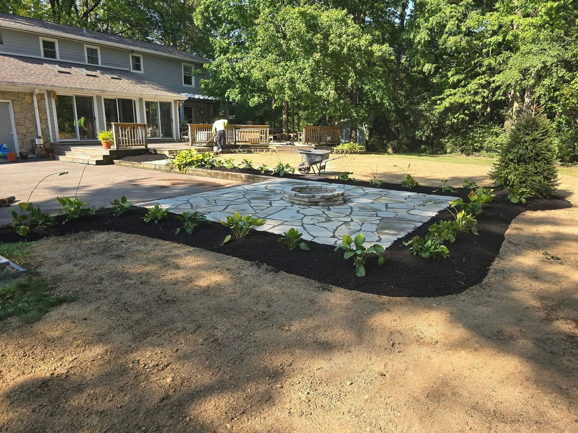 Backyard with stone patio, surrounded by mulch beds, and a two-story house.