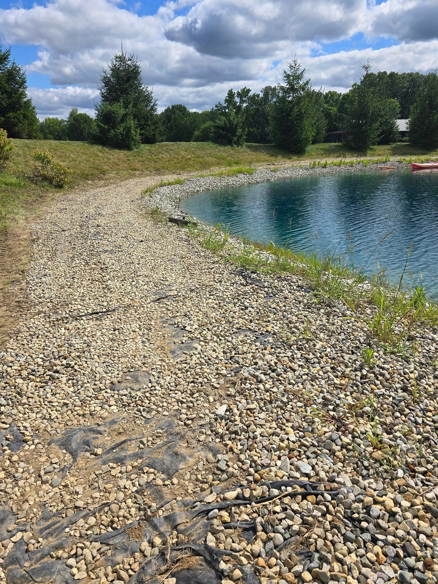 A pond's rocky shore with clear blue water under a cloudy sky.
