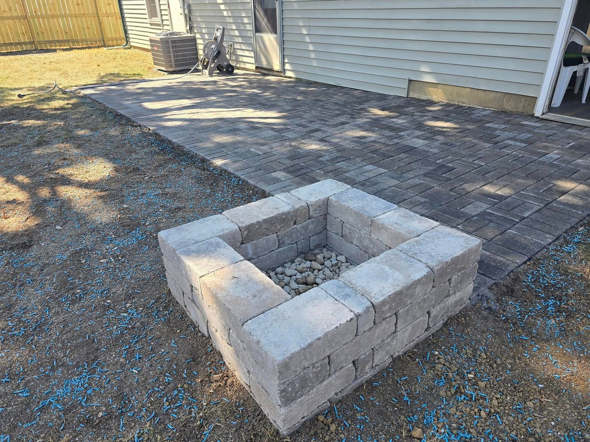 Square fire pit made of grey blocks on a gravel patio.