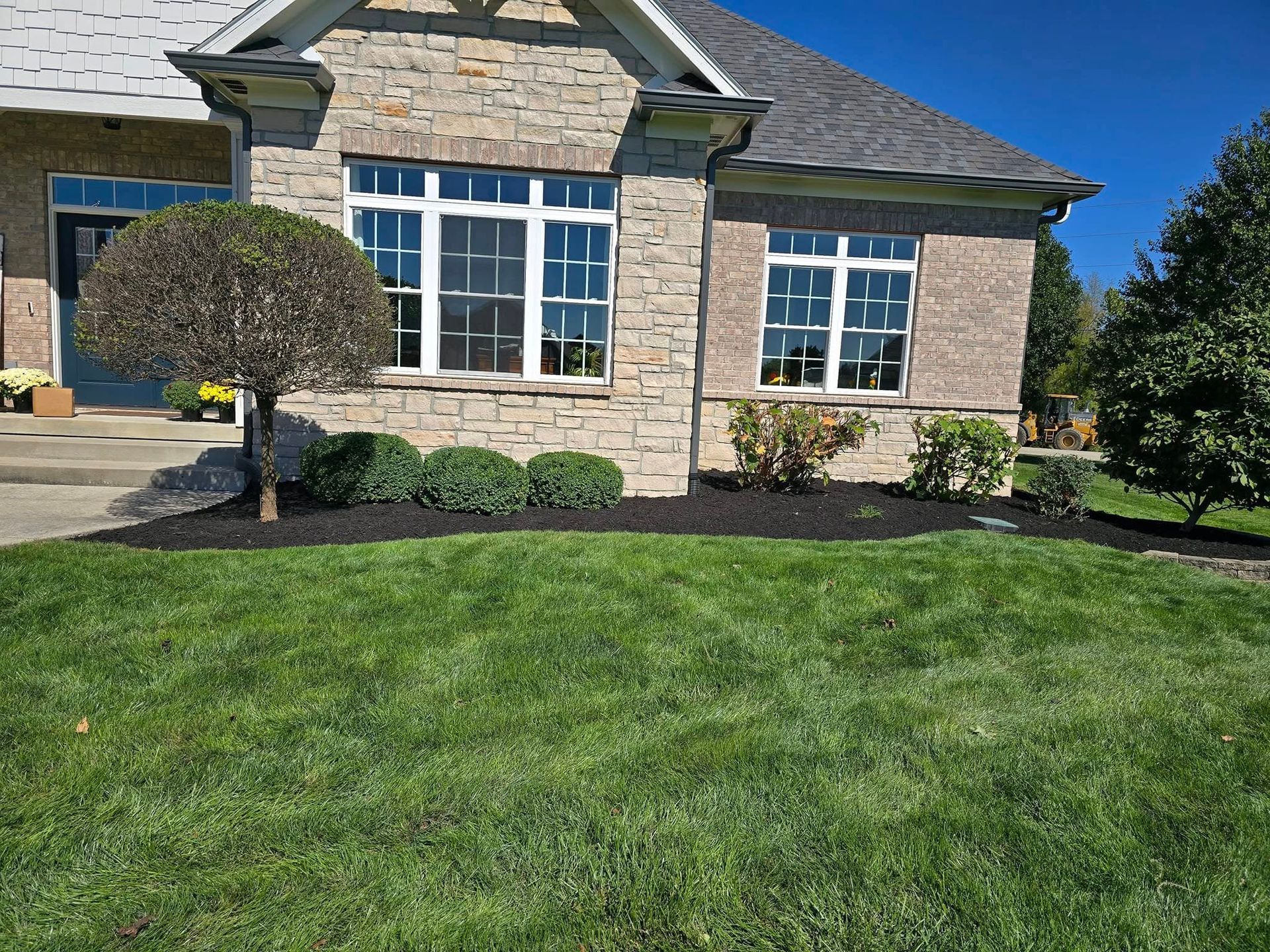 House with stone facade, windows, manicured lawn, and dark mulch around bushes.