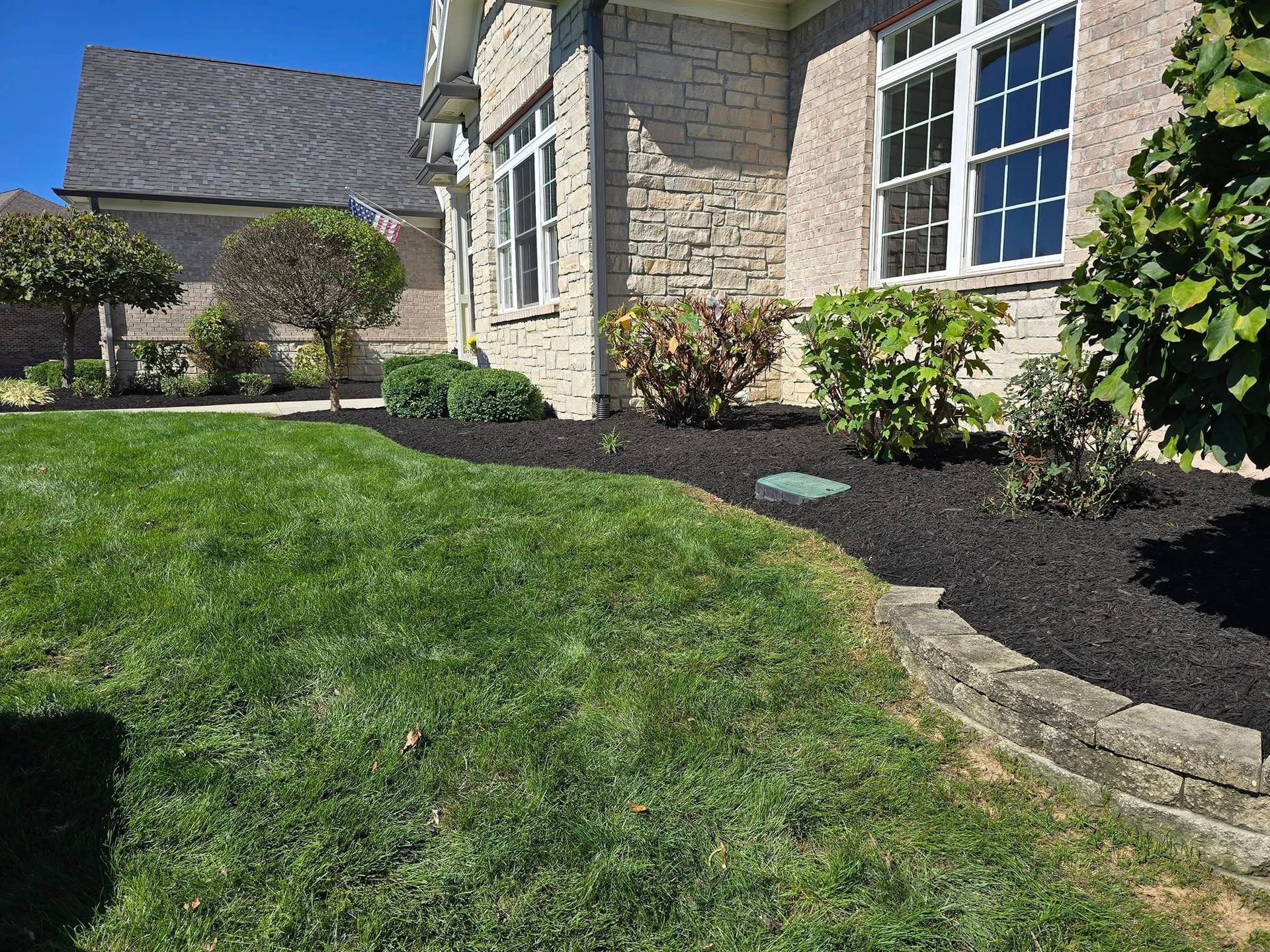 Lush green lawn with a flower bed edged with stone. A brick house is in the background.