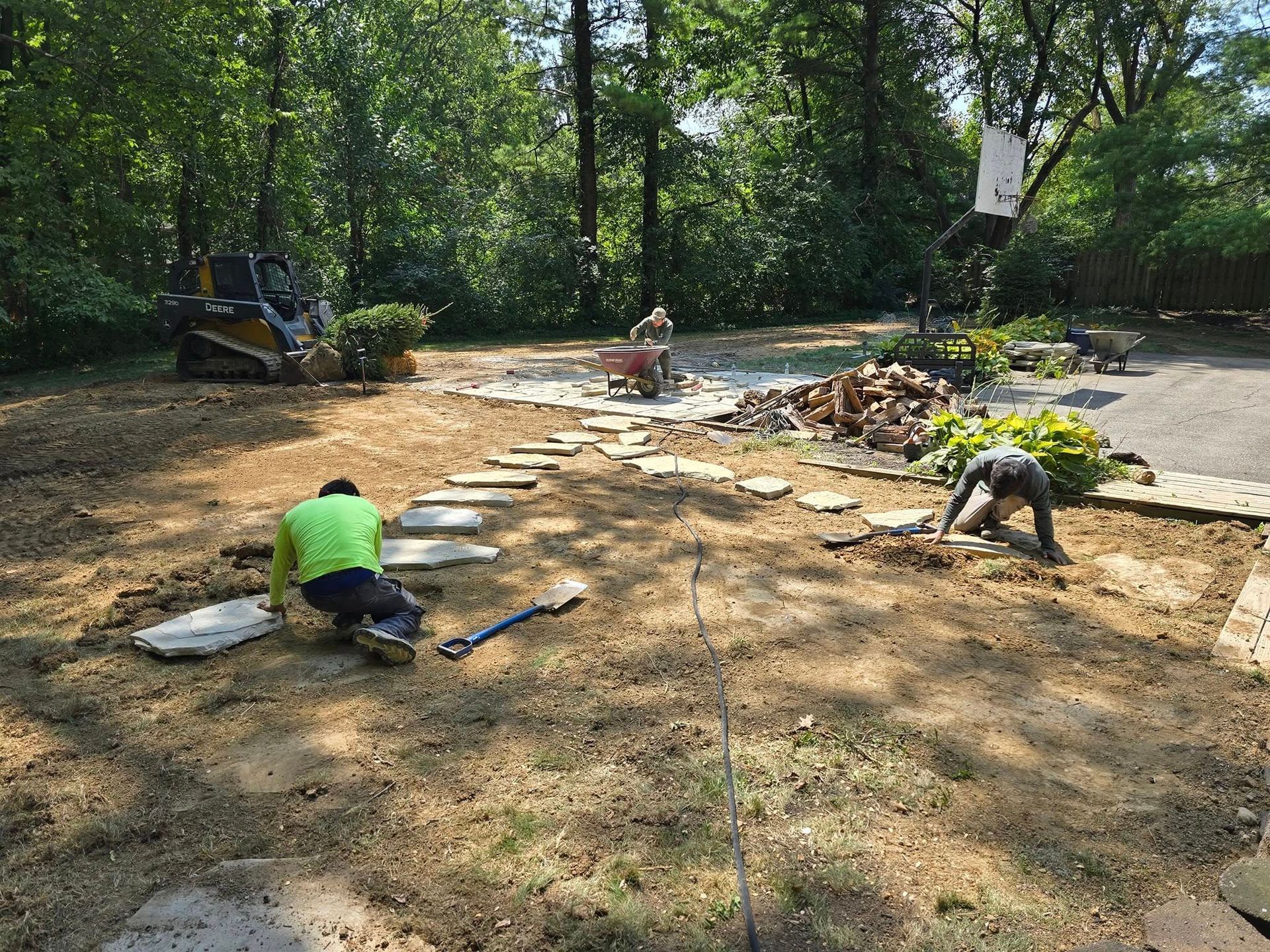 Landscapers laying stone path in yard with small excavator.