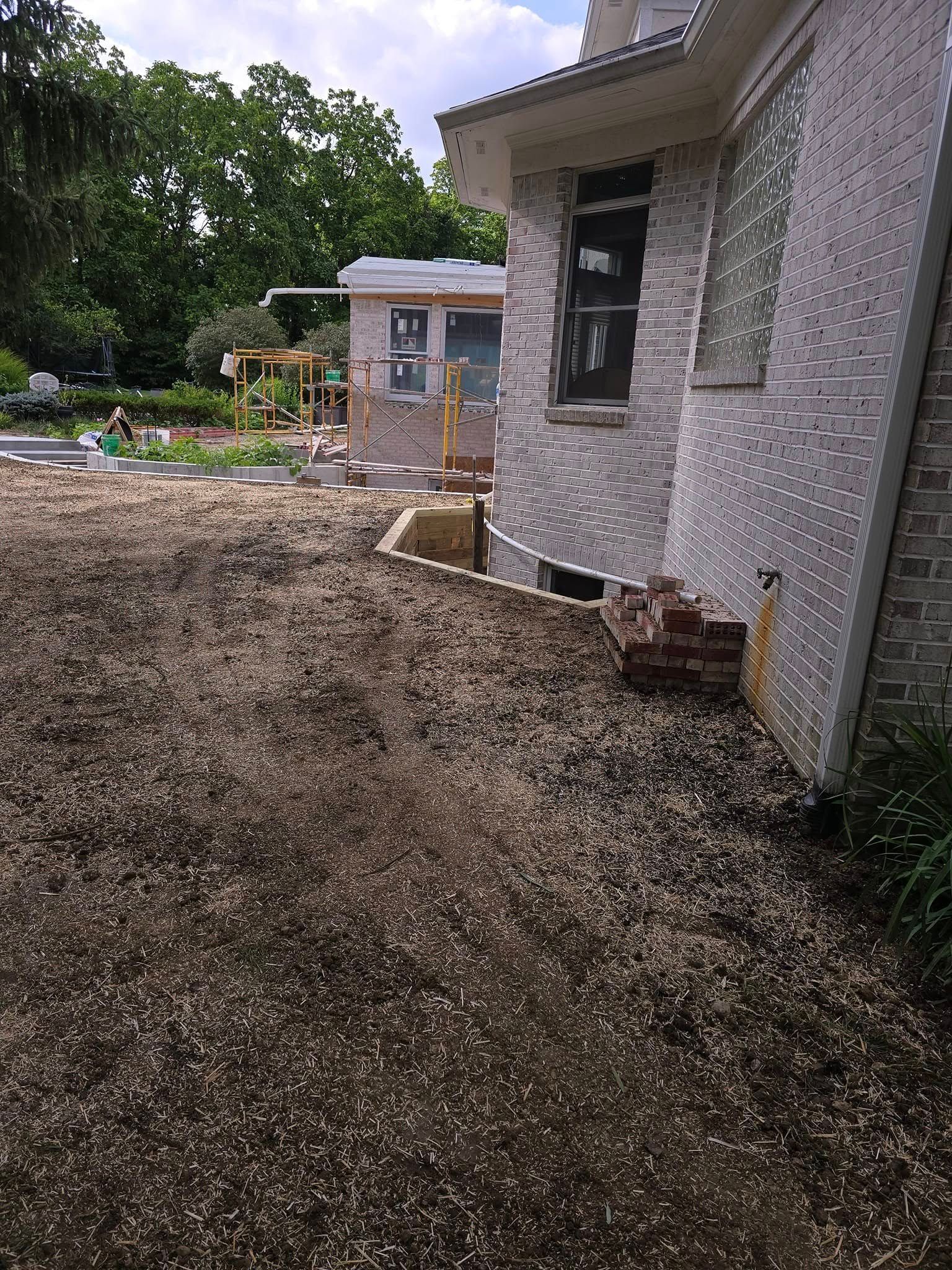 Exterior view of a brick house with a newly graded gravel area in the foreground and a garden in the background.