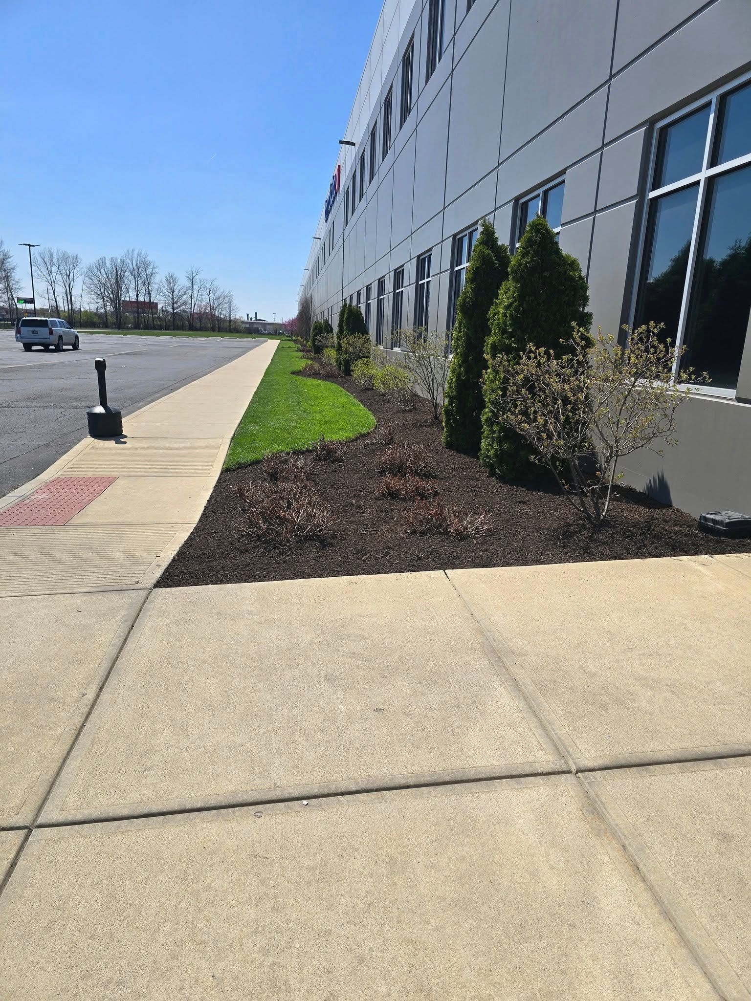Sidewalk next to a building with landscaping, a grassy area, and a sunny day.