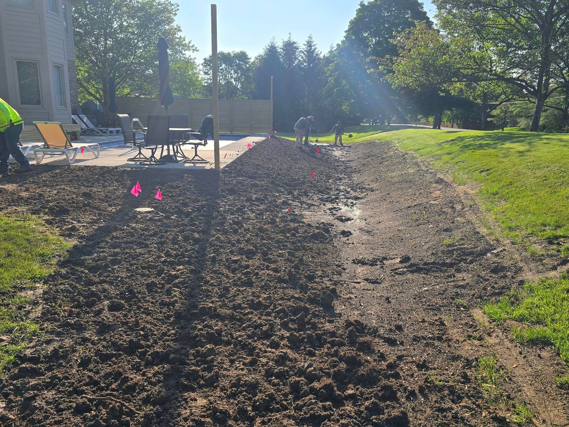 Workers preparing ground for landscaping next to a patio and lawn.