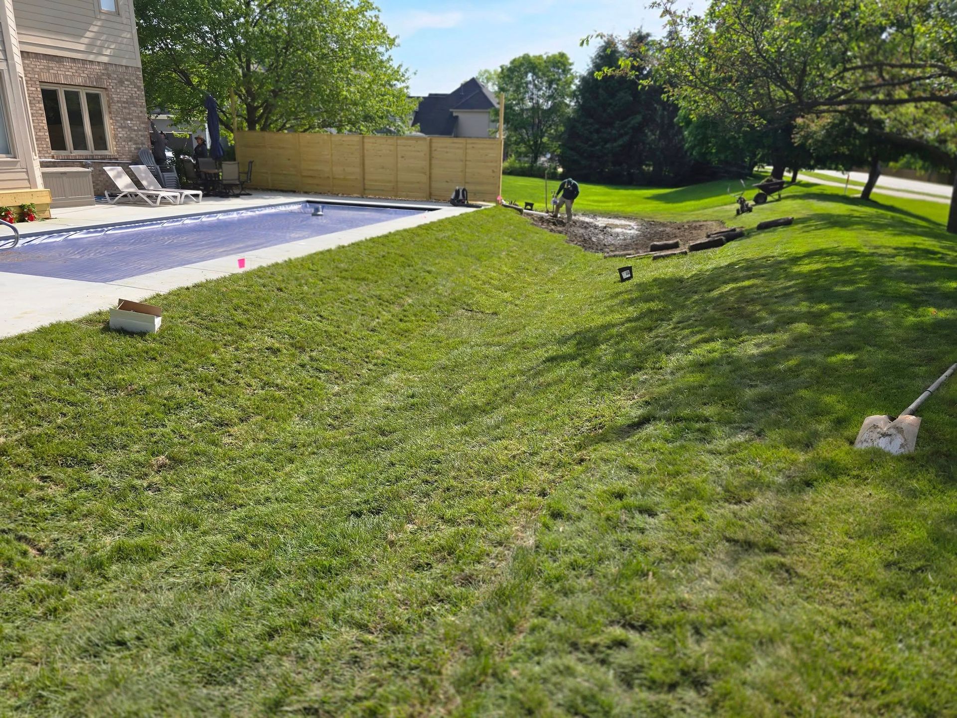Green lawn with a pool, fence, and person working on landscaping.