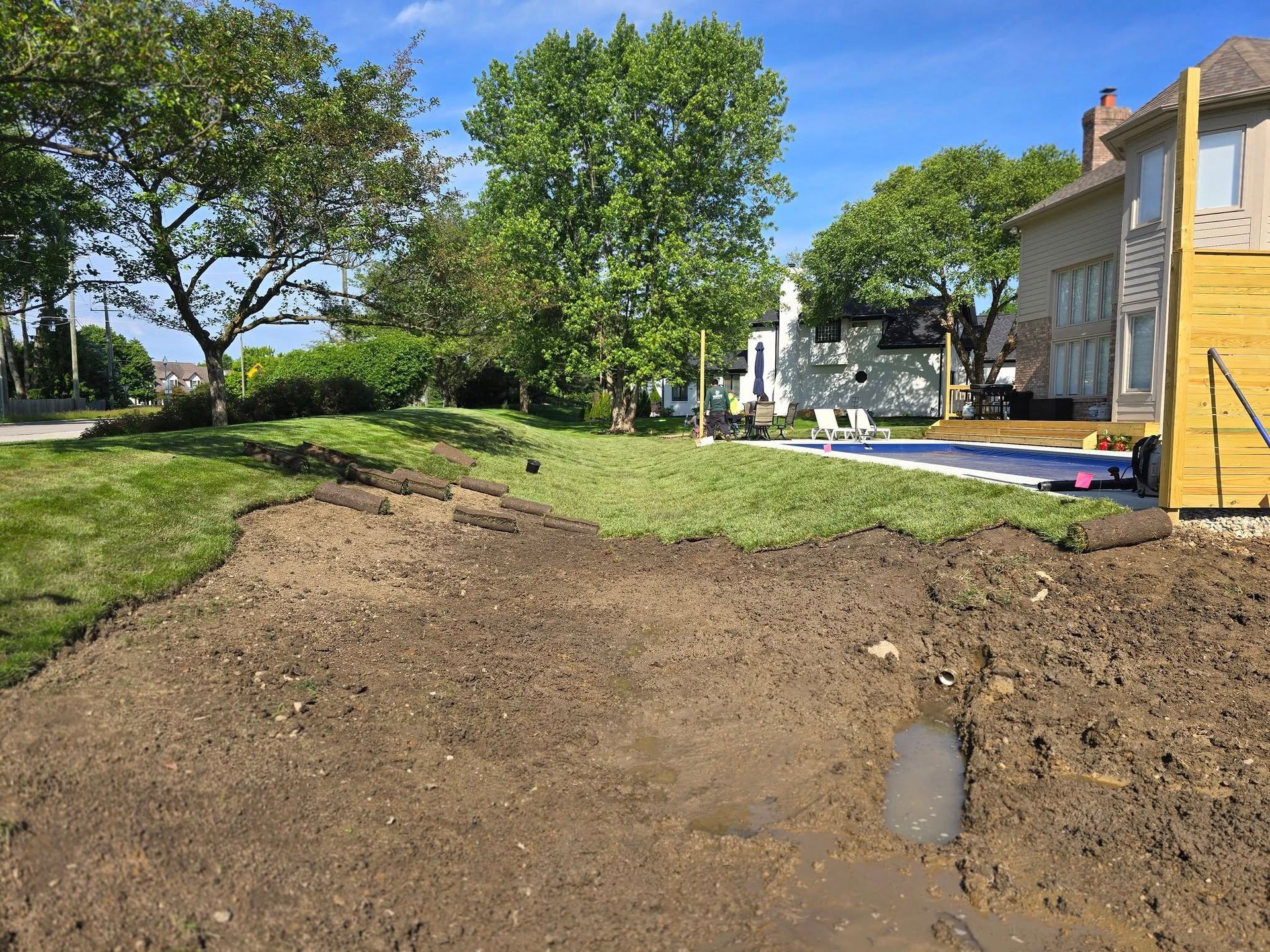 A yard under construction; dirt in foreground, grass, trees, and house.