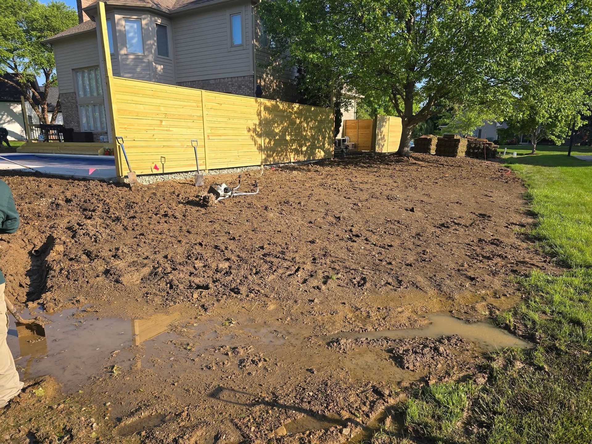 Muddy yard next to a house and fence; standing water and a small dog are visible.