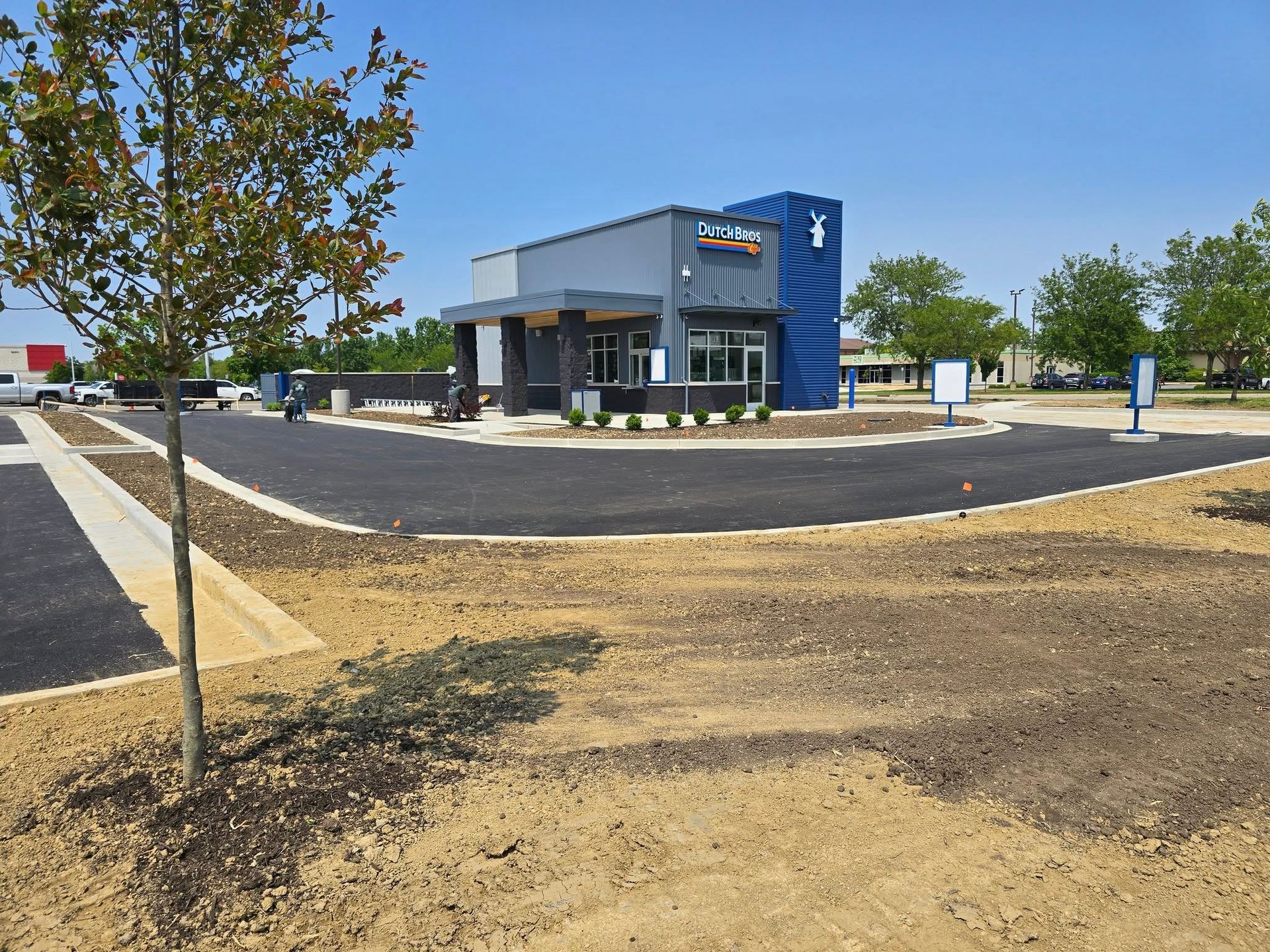 Drive-thru coffee shop; exterior view. Building with blue and gray exterior, newly paved drive-thru lane.