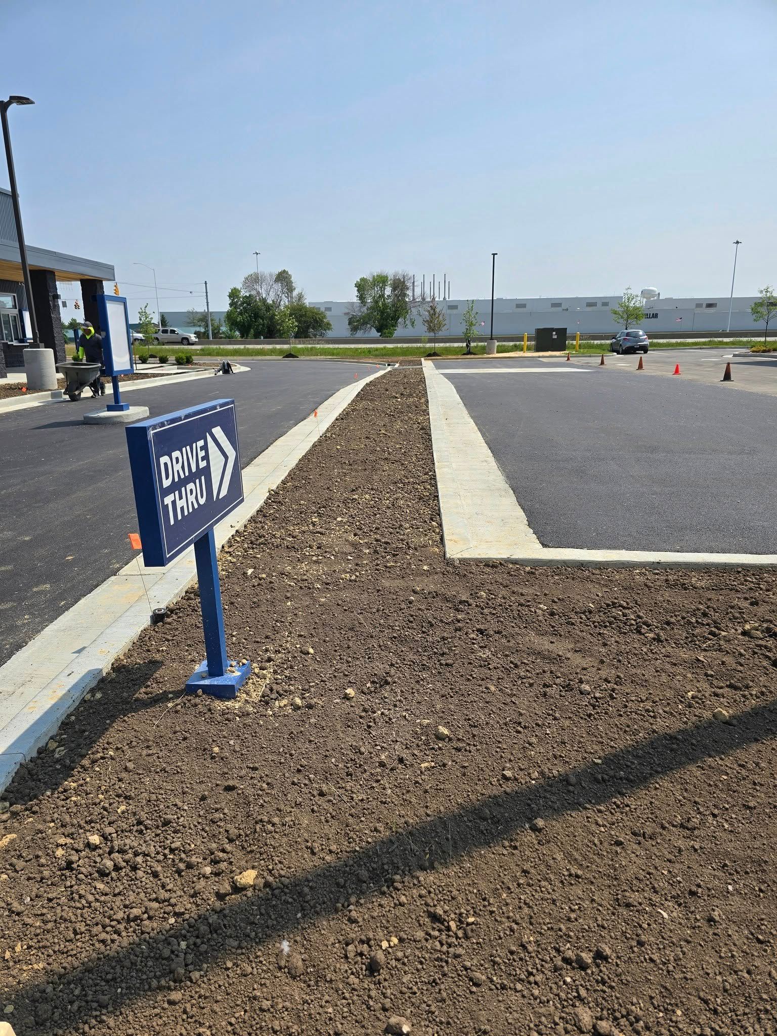 Drive-thru sign, blue, pointing right. Asphalt drive with gravel border. Sunny day, exterior shot.
