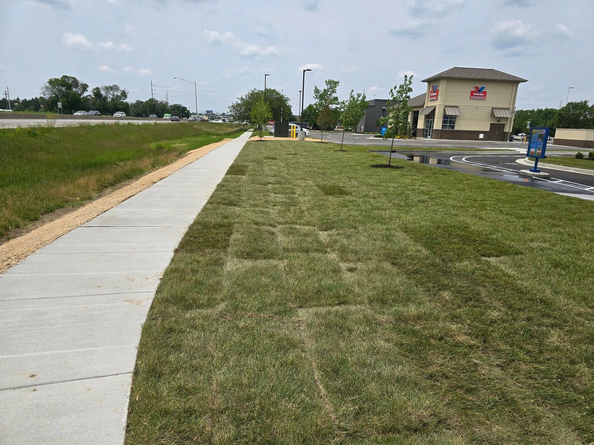 Sidewalk next to a grassy area with a building in the background.