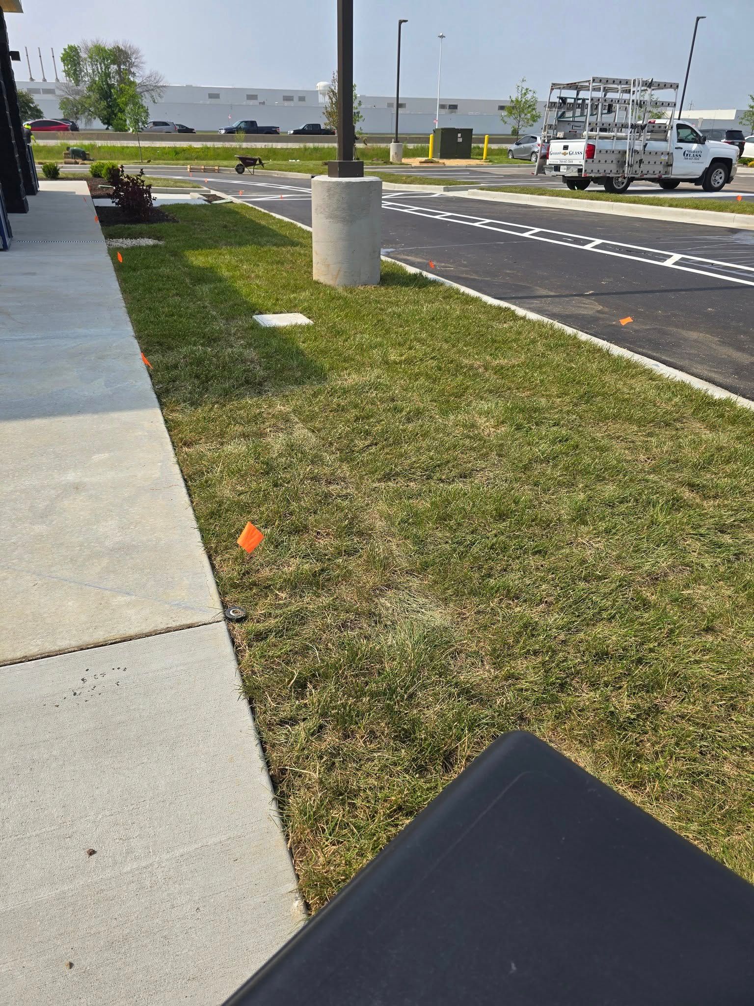 Grassy area next to a building and road, with a parking area and utility truck in the background.