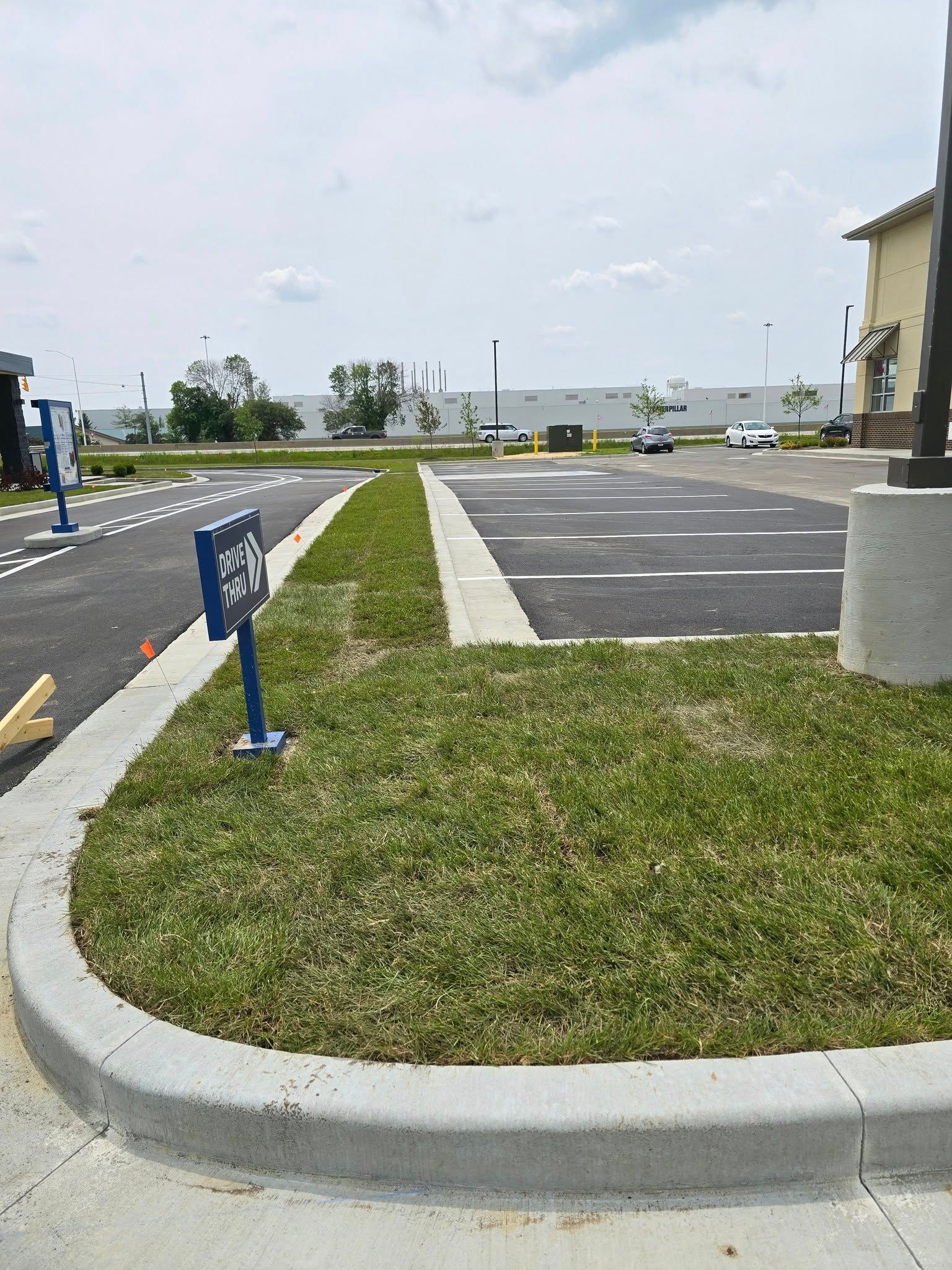 Parking lot with a grassy area and curb. Blue sign on the left.
