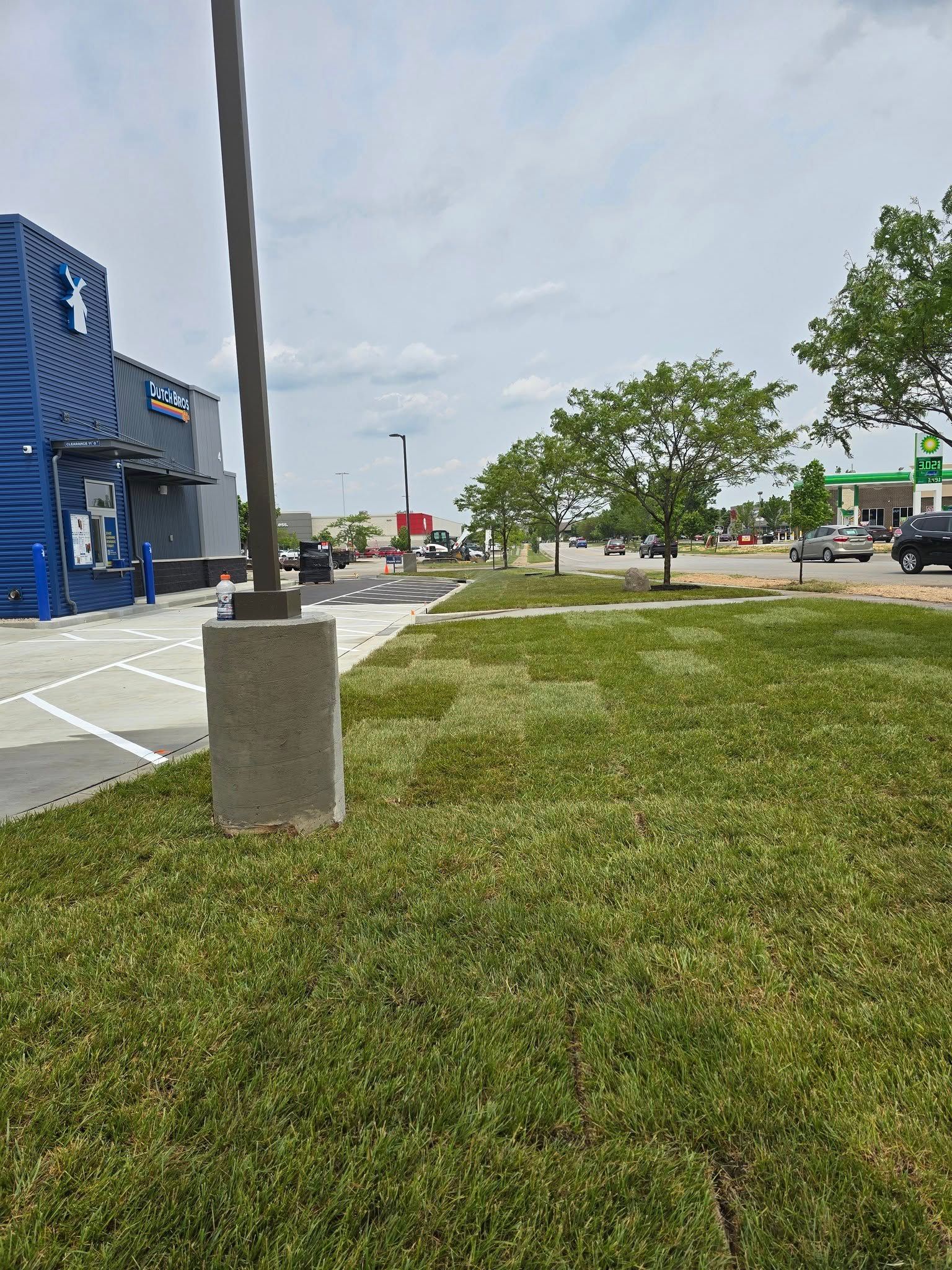 Grassy area with trees, road, vehicles, and a blue building with a star logo on a cloudy day.