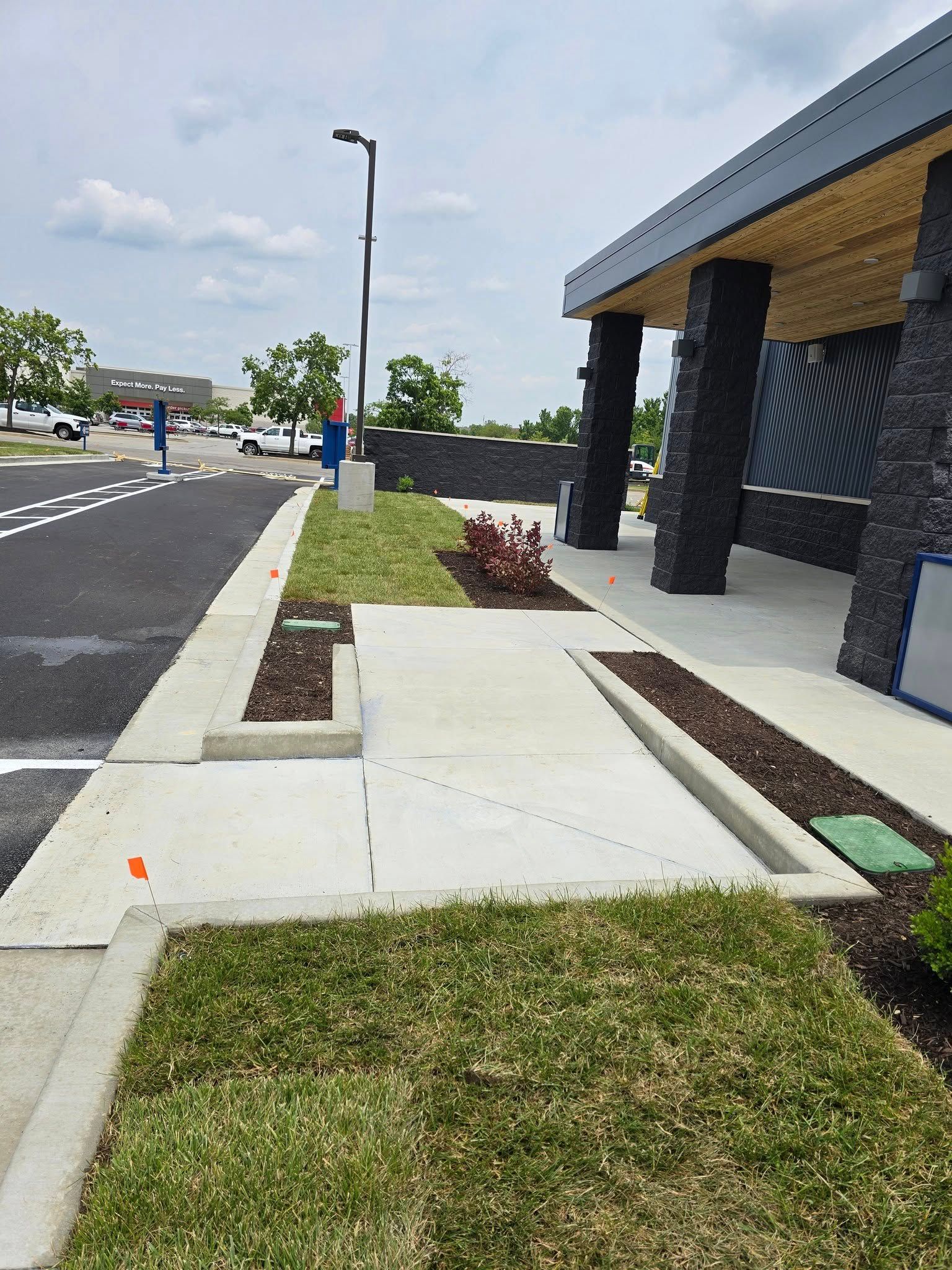 Concrete sidewalk with a ramp and landscaped areas in front of a building with dark columns.