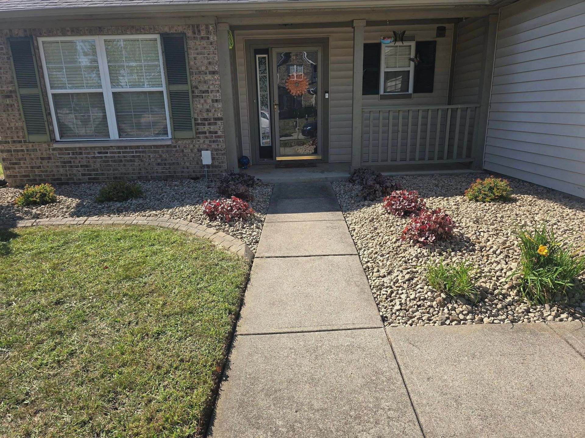 Front of a brick house with a concrete walkway leading to the front door, with landscaping and green grass.