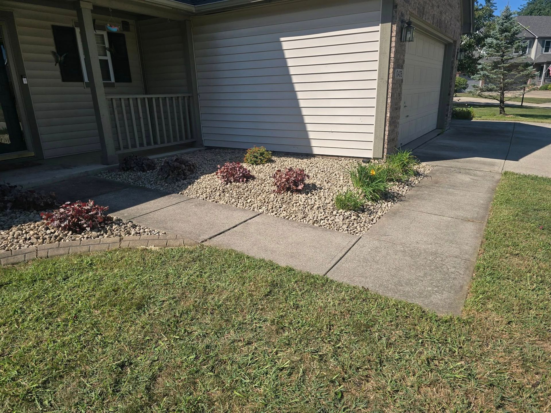 Concrete walkway leading to a house with landscaping, including plants and gravel, in front of the garage.