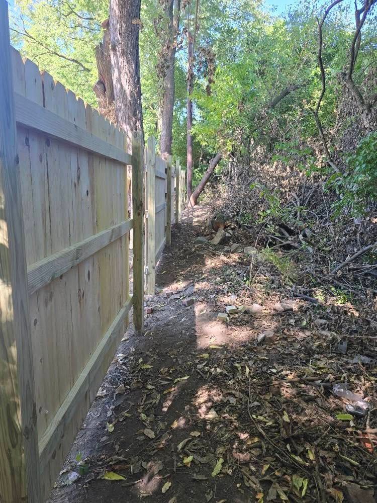 Wooden fence alongside a narrow dirt path through a wooded area.