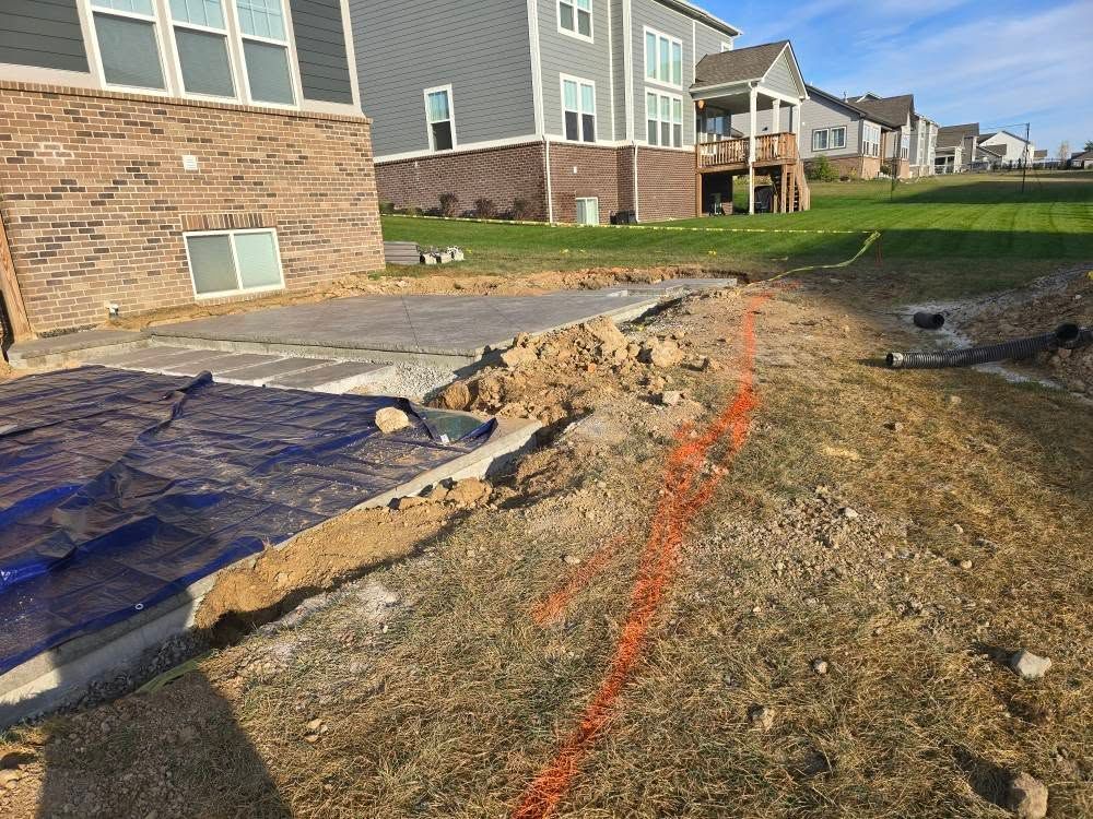 Construction site with exposed concrete, dirt, and orange markings in a residential area.