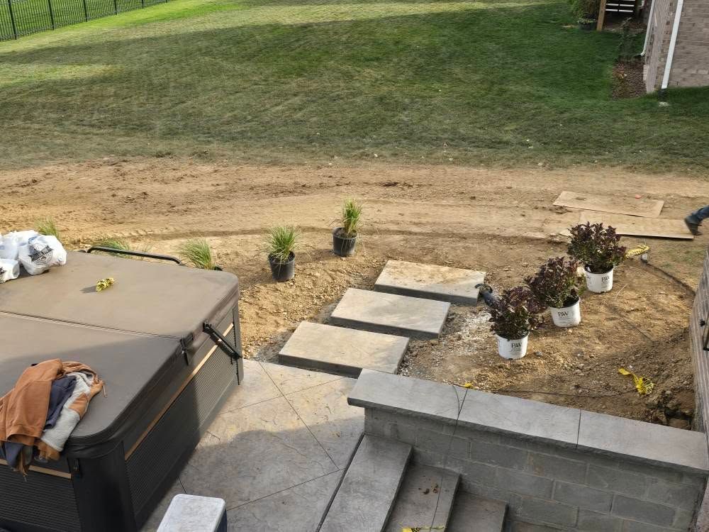Stone steps lead from a patio to a yard with new landscaping and a hot tub.