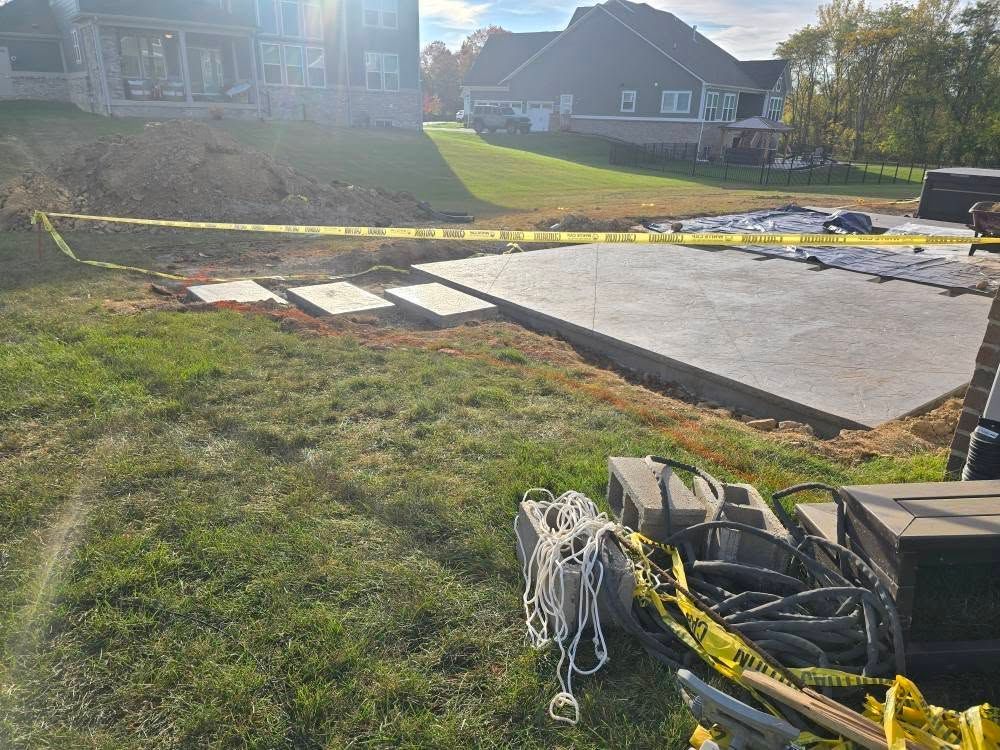 Construction site with a concrete patio. Yellow caution tape surrounds the area on a grassy lawn.