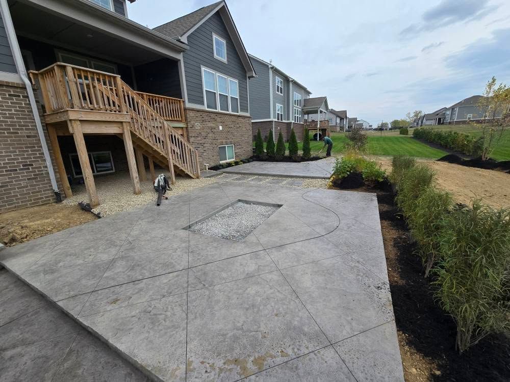 Concrete patio with steps, landscaping, and house in the background on a cloudy day.