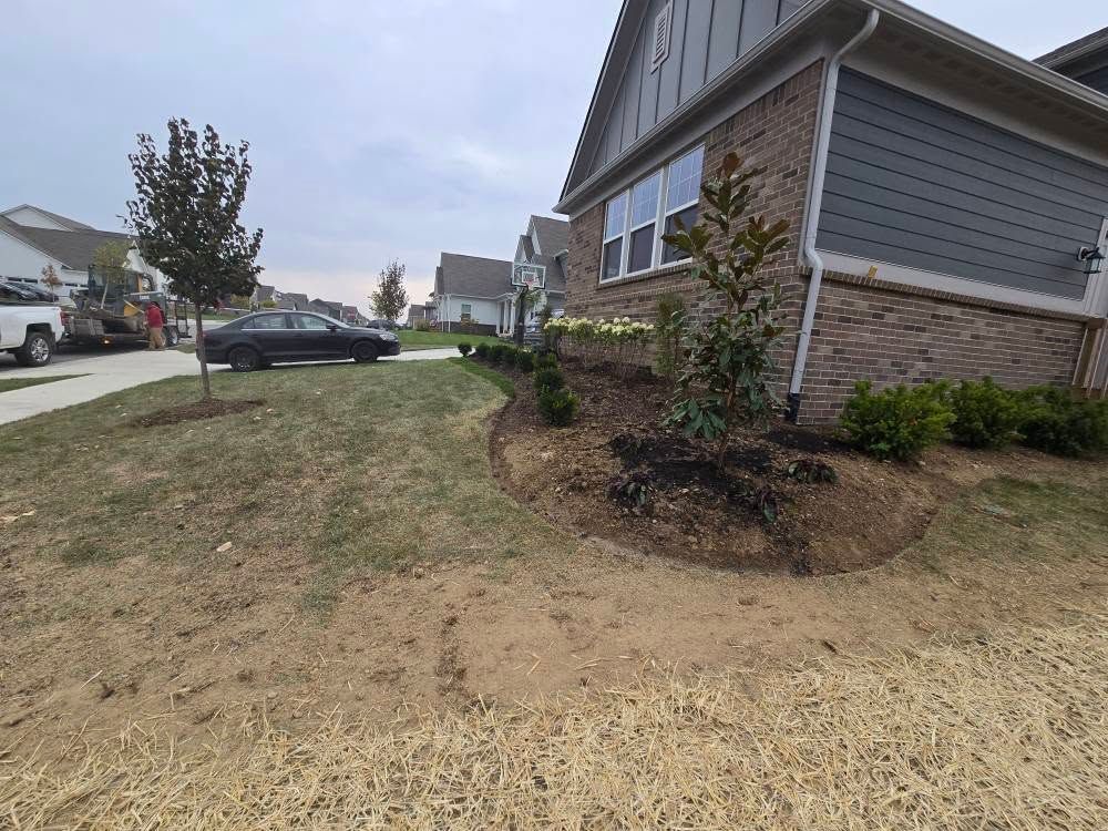 A suburban house with a landscaped garden bed and a brown lawn under an overcast sky.
