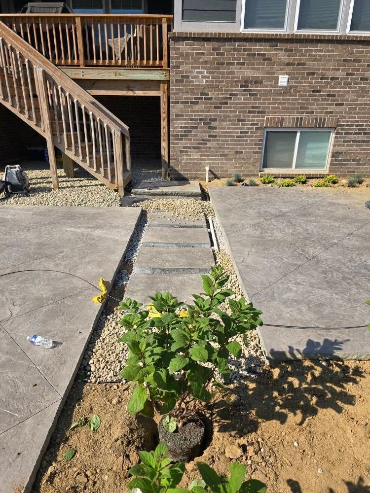 A concrete patio with steps leading to a deck. A small garden is in the foreground.