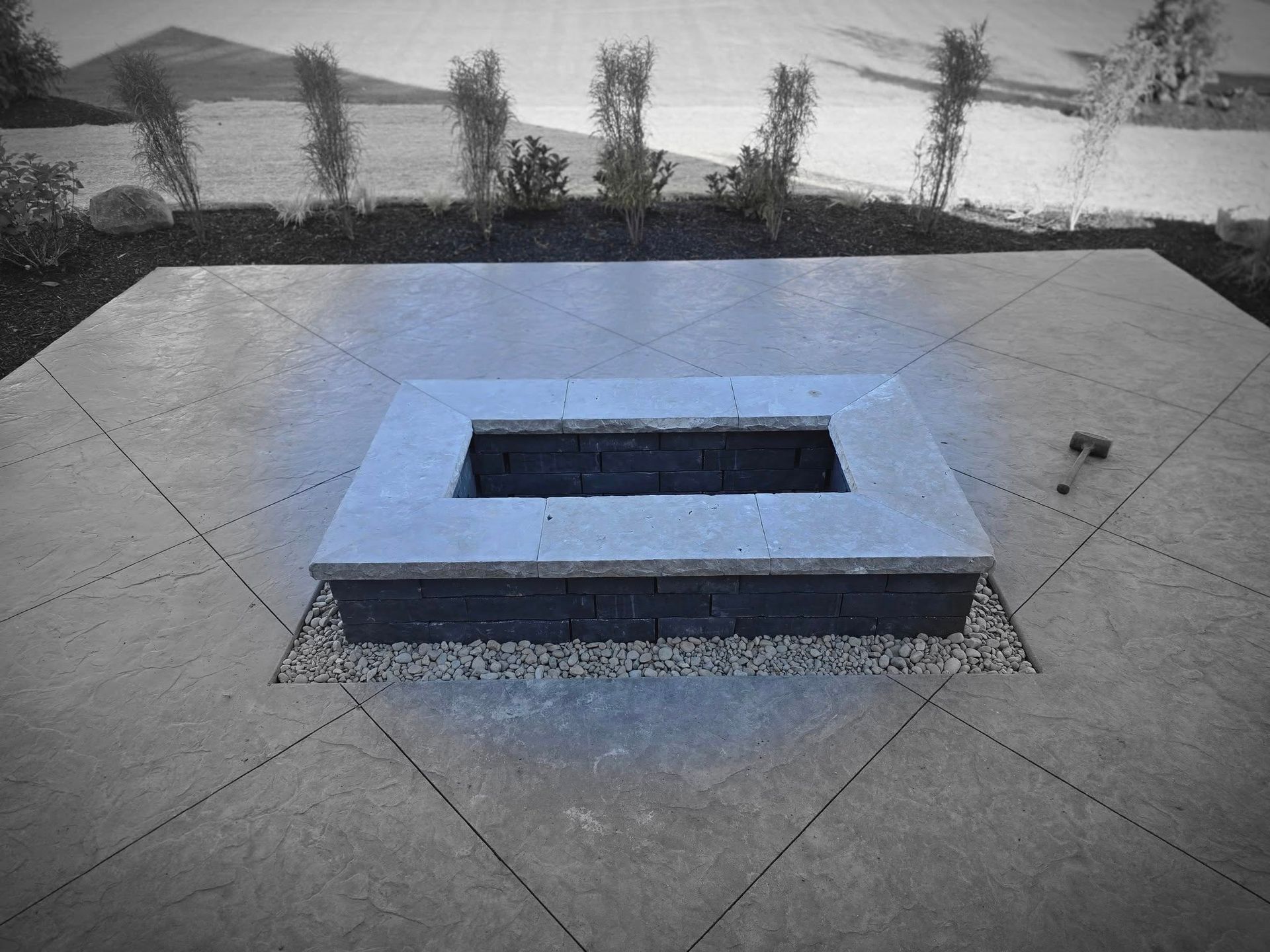 A rectangular fire pit with a concrete border sits on a gray stone patio.