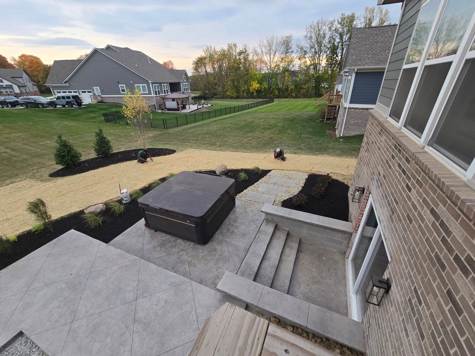 Backyard with hot tub on a concrete patio, landscaping, and house with brick exterior.