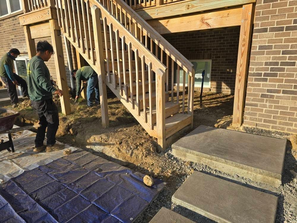 Workers landscaping under a wooden deck with stairs. Two concrete steps are in foreground.